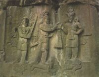 Relief from Taq-i Bostan showing Ardashir II at the center receiving his crown from Ahura Mazda. The two stand on a prostrate enemy. At the left is Mithra as a priest, wearing a crown of sun-rays, holding a priest's barsam, and standing on a sacred lotus.