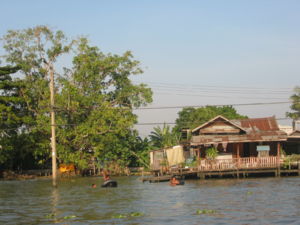 A Bangkok canal with a home and residents swimming.