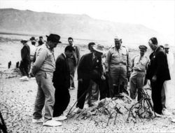 Oppenheimer, Groves, and others at the site of the Trinity test shortly after the bombings of Hiroshima and Nagasaki.