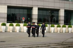 Policemen in black uniform marching towards the poles near the Golden Bauhinia Square, with their hands holding both the regional and national flags. A flag-raising ceremony is held there every day at 8:00 a.m.