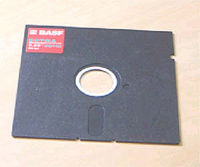 A 5¼-inch disk with a partly exposed magnetic medium spun about a central hub. The cover has a cloth liner to brush dust from the medium. Note the "write-enable slot" to the upper right and the strobe hole next to the hub that regulates drive speed.