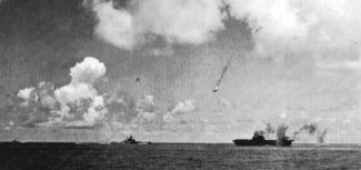 A Japanese Val dive bomber (center) is shot down during the attack on the Enterprise (lower right).  Enterprise is smoking from earlier bomb hits as another bomb near-misses the carrier.