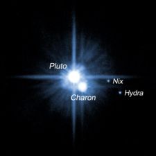 Pluto and its three known moons. Pluto and Charon are the bright objects in the center, the two smaller moons are at the right and bottom, farther out.