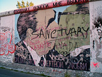 An image on the Berlin Wall of Leonid Brezhnev and Erich Honecker making out. The words at the top read "God! Help me stay alive" and continue at the bottom "Among this deadly love"