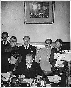 Soviet Foreign Minister Vyacheslav Molotov signs the Molotov-Ribbentrop Pact.  Behind him stand (left) German Foreign Minister Joachim von Ribbentrop and (right) Soviet Premier Joseph Stalin.