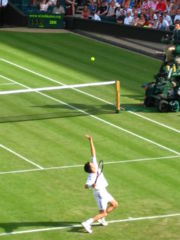 Tim Henman preparing to hit a serve. The left arm is extended, having just launched the ball into the air. The right arm will be raised up and forward at speed so that the racket connects with the ball.