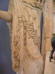 Swastika-type designs on the peplos of an Archaic kore, Acropolis Museum. The intersections of lines defining a solid repeated motif on the edge of a depicted piece of cloth resemble a swastika.