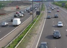 The M25 motorway looking south between junctions 14 and 15, near Heathrow Airport. The red light from the overhead gantry, just visible in the distance, is the MIDAS system indicating a reduced speed limit due to congestion