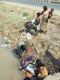 Women washing clothes in ditch alongside main road in Mumbai, India.