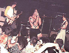 Black Flag performing in 1984. Left to right: Greg Ginn, Henry Rollins, and Kira Roessler. Drummer Bill Stevenson is not visible behind Rollins.