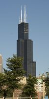 Distant ground-level view of a 110-story building with a black steel exterior and dark windows; the building has setbacks at several levels, and two large antennas rise above its roof.