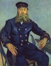 a long-bearded man with a blue uniform and hat is seated in a chair facing forward with his right arm on the chair's arm and left arm on a table and with a pastel blue background