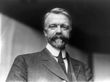 A black-and-white of a man with a mustache wearing a suit and a tie