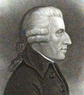 A profile view of a pleasant faced clean shaven man in his 50s or 60s with a strong nose. He is wearing a gray wig with a pigtail and side-rolls, and a jacket with a large collar and buttons.