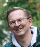 Head shot of a smiling man with glasses outdoors.