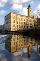 A stone factory stands against a vivid blue sky, its reflection mirrored in the waters below.