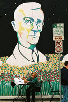 Wall mural depicting a man, with glasses in a suit and tie, in a field of flowers. A lady at a cafe table sits in front of the mural