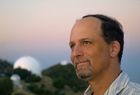 A white man wearing a shirt looking left, with an observatory on the left side of the picture