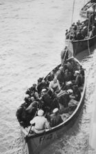 Photograph looking down on two lifeboats crammed with people in naval uniforms. A third lifeboat of a different design can be seen behind the first two.