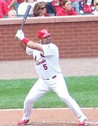 Baseball batter in a red hat, white top and white pants, batting for the Cardinals.