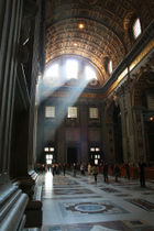 The main doors with light streaming in can be seen at the end of the nave. The enormous space dwarfs the people who are walking across the shining tiled floor.