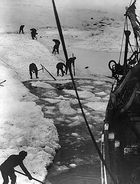  Men with digging tools removing ice surrounding the ship's hull, creating an icy pool of water