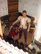 A wax figure of a man stands, preparing for battle.  The figure sports a bowl cut and wears a khaki doublet and dark brown breeches.  At its legs is the wax figure of a kneeling squire.