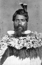 Man wearing traditional Māori cloak with two feathers in his hair