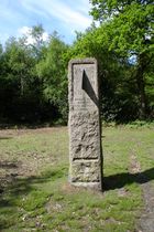 A standing stone in a grassy field surrounded by trees. The stone contains a vertical sundial centered on 1 o'clock, and is inscribed "HORAS NON NUMERO NISI ÆSTIVAS" and "SUMMER TIME ACT 1925".