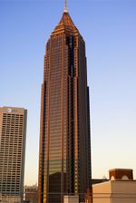 Ground-level of a 50-story building with a reddish exterior; the building is capped by a pyramidal, latticework structure that tapers into a large spire.