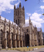 Large yellow stone ornate building with buttresses and square central tower.