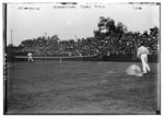 Two players in white pants and shirts playing on a grass court in front of a small crowd