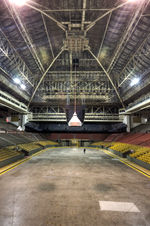 The interior of an arena. There are bands of seats of different colours, and there is a high, vaulted ceiling.