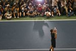 A man in black shorts and a black short kisses a silver trophy, with dozens of photographers taking photos of him in the background