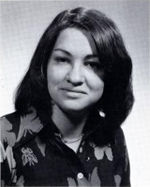 A formal pose of a young woman in her early twenties, dark straight hair parted near the center, wearing a dark floral print top.