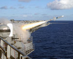 Firing of a missile from Roosevelt while at sea, seen from the flight deck. There is a Phalanx cannon on the left, with a white, domed upper section and a black cannon on the lower part.