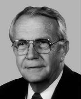 A graying man in his fifties, facing left, wearing glasses and a suit and tie