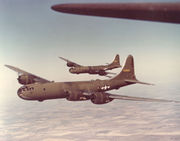 Two large, olive-colored airplanes flying over farmland.