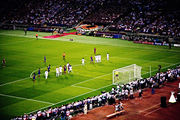 A wide-angle photograph of several football players preparing for a free-kick to be taken.