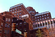 A red brick high-rise building with several wings and levels in front of a bright blue sky with a traffic light and street sign visible at the bottom.