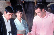 Upper body shot of two men and a woman in a kimono, looking down.