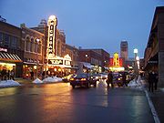 City street at night with snow on the sidewalks. The signs for the Michigan Theater (on the left) and State Theater (in the center and further down the street) are brightly lit