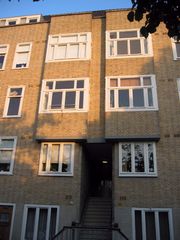 A four story, brick apartment block showing the building's facade, with several windows and an internal staircase leading into the block.