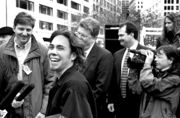 A black and white photo featuring a joyous man with a large smile who is giving an interview to a group of smiling news reporters that are crowded around him.