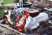 Aerial view of a large city building. The building is composed of oddly-shaped, metallic sections. Curved glass and metal pieces run along the face of the building.