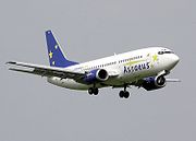 A mostly white aircraft, with blue nacelles and tail, is shown in the air, seemingly approaching a runway for landing. The aircraft is facing the right of the image with its landing gear down. Two engines are seen in their nacelles.