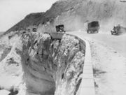 A road at the edge of a cliff with trucks driving both ways along it.