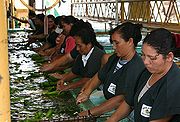 Photo of long row of women sitting at table, working with bananas