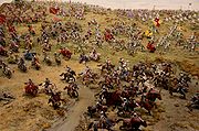 Miniatures of knights, archers, and infantry on tufted sand depict an instance of the battle.