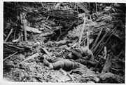 In the foreground the limp bodies of dead German soldiers lie amidst the rubble of a destroyed trench. It is difficult to distinguish the soldiers from the rubble around them, but three bodies are clearly visible. One man, wearing a helmet, has been pushed forward by the blast and, although dead, appears to crouch forward.